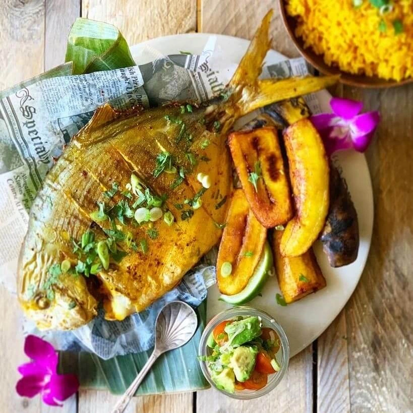 A plate of a grilled fish seasoned with scallions and a bowl of yellow rice.
